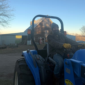 Person sitting on a blue tractor in front of a barn and building.